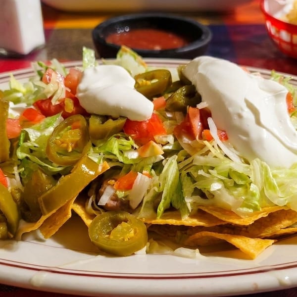 A plate of nachos with lettuce, tomatoes, jalapeños, and sour cream on a colorful tablecloth.