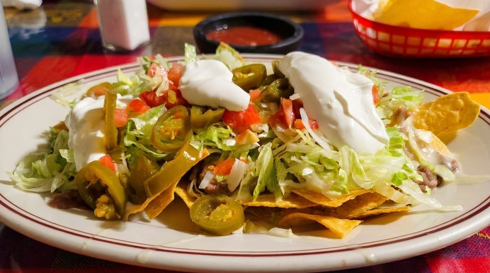 A plate of nachos with lettuce, tomatoes, jalapeños, and sour cream on a colorful tablecloth.