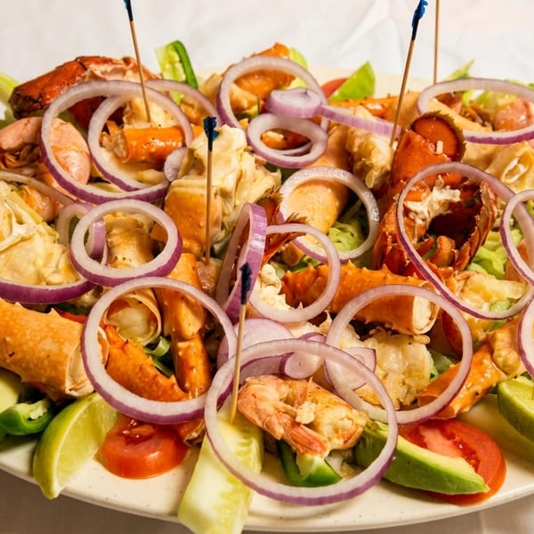 A vibrant seafood platter with lobster, shrimp, crab, red onion, tomatoes, and lime wedges.