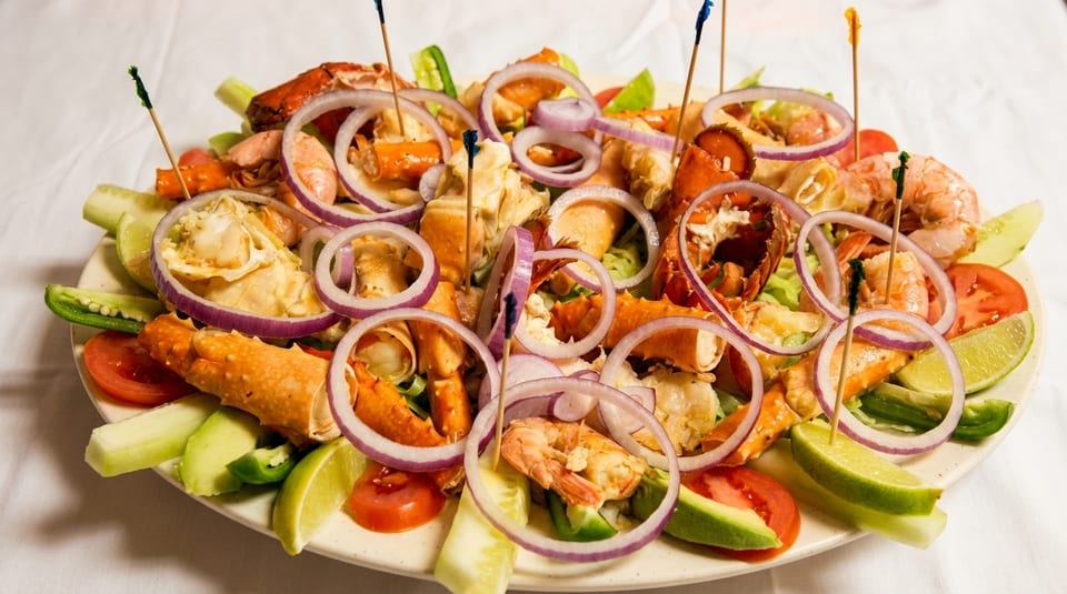 A vibrant seafood platter with lobster, shrimp, crab, red onion, tomatoes, and lime wedges.
