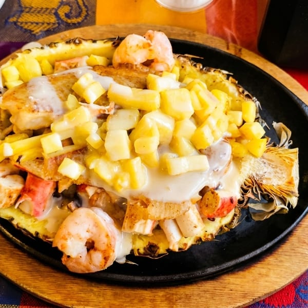Seafood and pineapple dish served in a pineapple half on a sizzling skillet.