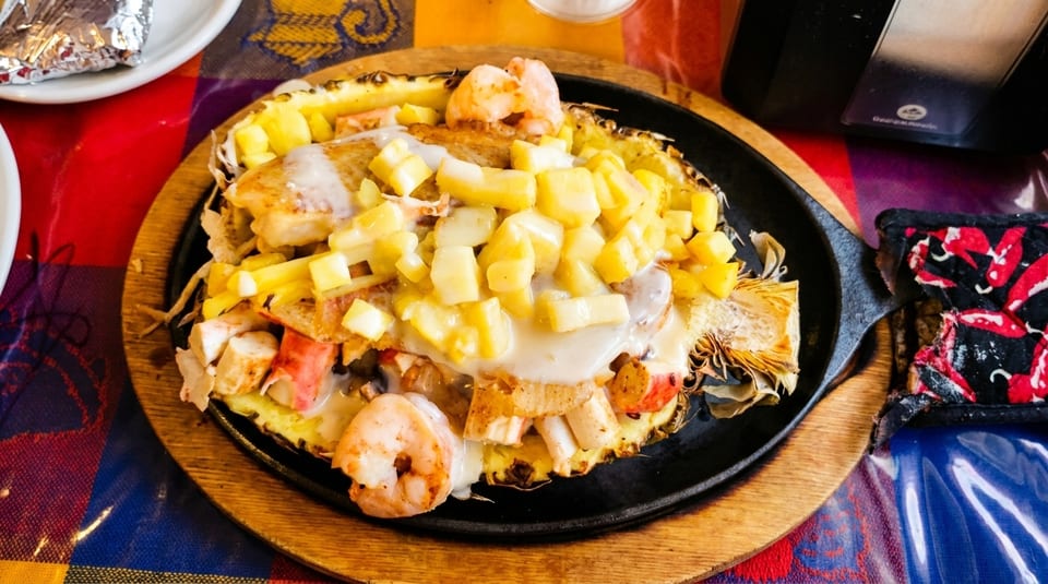 Seafood and pineapple dish served in a pineapple half on a sizzling skillet.